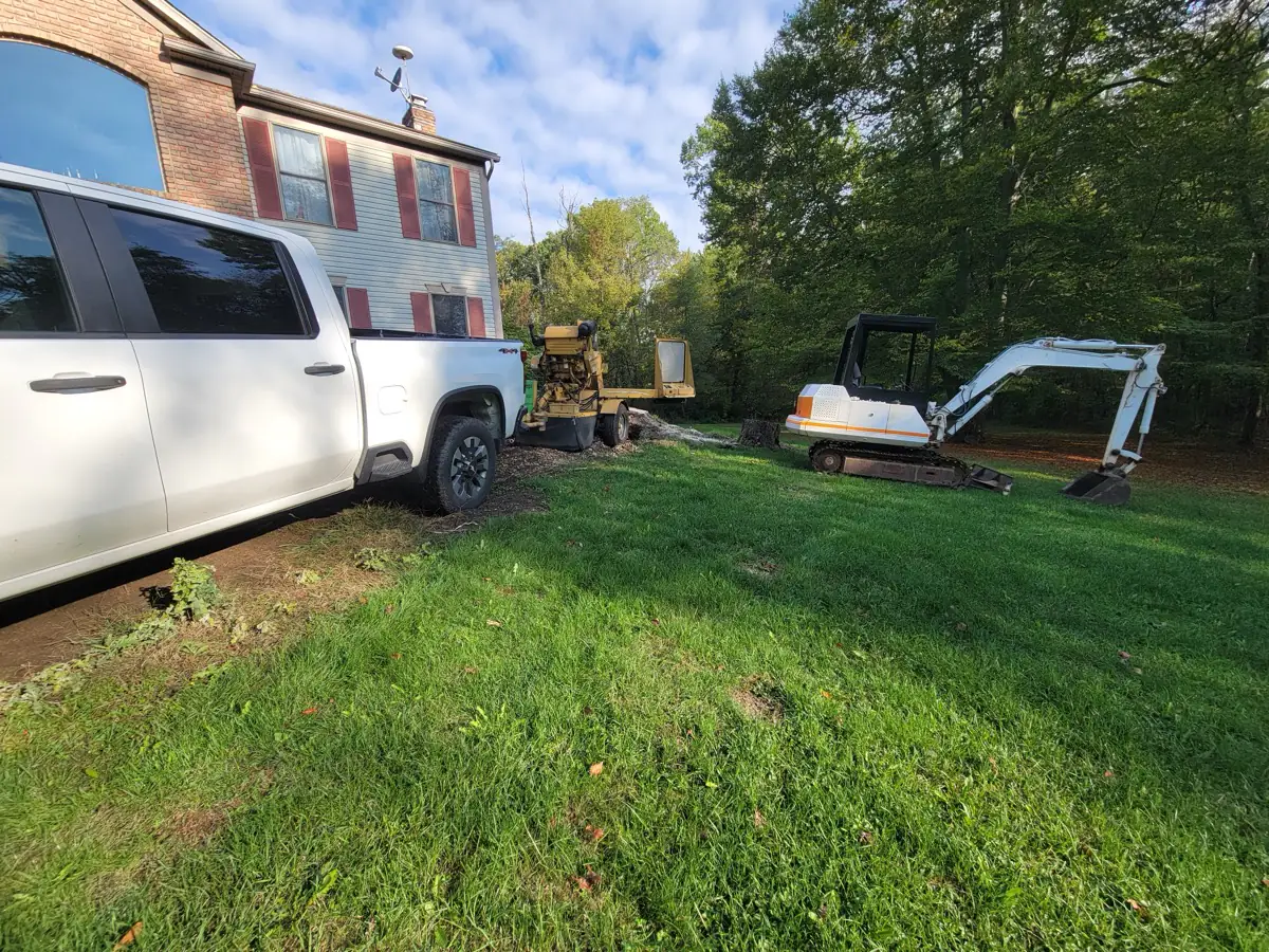 Stump grinder and mini excavator staged beside a truck at a customer’s home